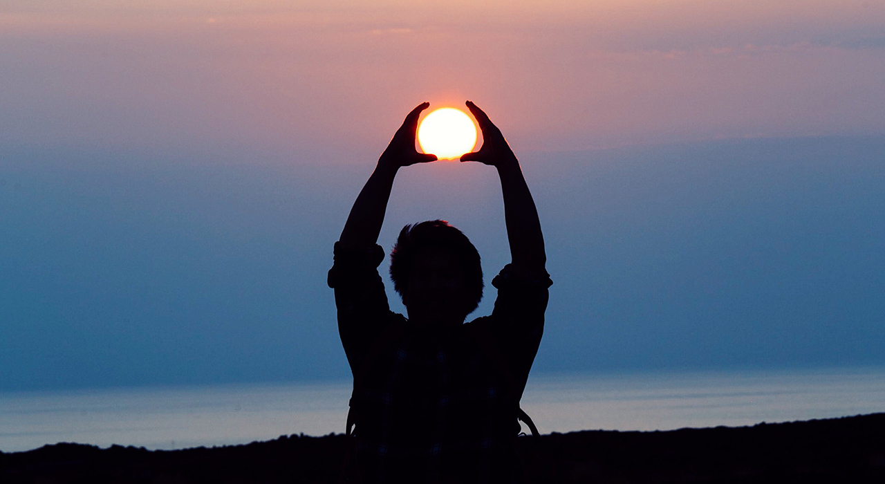 手で作った輪の中に収まる夕日